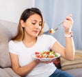 Peruvian housewoman eating vegetable salad on sofa at home