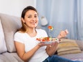 Peruvian housewoman eating vegetable salad on sofa at home