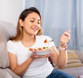 Peruvian housewoman eating vegetable salad on sofa at home