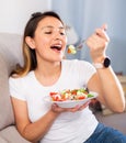 Peruvian housewoman eating vegetable salad on sofa at home