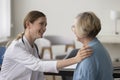 Positive physician woman talking to elderly patient, touching shoulder Royalty Free Stock Photo