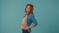 Positive pregnant woman measures her belly with a tape and smile while standing against a blue background. Healthy Royalty Free Stock Photo