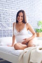 Positive pregnant woman sitting on bed, holding belly Royalty Free Stock Photo