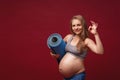 Positive pregnant woman in sports clothes holds a gym Mat in her hands