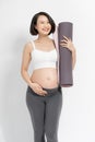 Positive pregnant woman in sports clothes holds a gym Mat in her hands