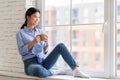 Positive pretty asian woman sitting on window, drinking coffee Royalty Free Stock Photo