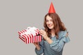 Positive pretty girl with funny party hat opening gift box looking at camera, smiling satisfied with present, enjoying birthday Royalty Free Stock Photo