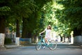 Positive pretty girl in white dress and straw hat is happy riding blue bike down wide beautiful park alley