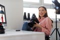 Positive pretty lady photographer working in studio, sitting at workdesk with computer, holding professional camera Royalty Free Stock Photo
