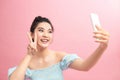 Positive pretty woman holding camera with extended arm, showing peace sign, taking selfie on smartphone with carefree smile Royalty Free Stock Photo