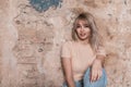 Positive pretty young woman sits and funny smiling near a vintage brick wall in the studio. Cheerful pretty fashionable girl model