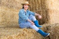 Positive relaxed asian female farmer resting on hayloft after work at farm, sitting on straw stack and smiling Royalty Free Stock Photo