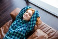 Positive relaxed redhead girl resting on brown leather couch