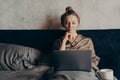 Positive relaxed young woman in pajama lying in bed and using laptop