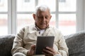 Positive retired man relaxing on comfy couch using tablet computer