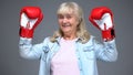 Positive retiree woman in boxing gloves rising hands up, success concept, belief