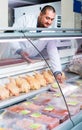 Male shop assistant selling kosher chicken at counter and smiling