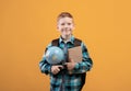 Positive schoolboy with backpack holding heap of books and globe Royalty Free Stock Photo