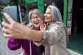 Positive senior Asian lady with grey haired friend take selfie on modern city street Royalty Free Stock Photo