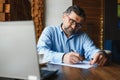 Positive senior bearded man with grey hair drinking coffee and using laptop at cafe, copy space. Stylish aged Royalty Free Stock Photo