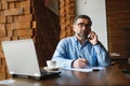 Positive senior bearded man with grey hair drinking coffee and using laptop at cafe, copy space. Stylish aged Royalty Free Stock Photo