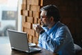 Positive senior bearded man with grey hair drinking coffee and using laptop at cafe, copy space. Stylish aged Royalty Free Stock Photo