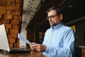 Positive senior bearded man with grey hair drinking coffee and using laptop at cafe, copy space. Stylish aged Royalty Free Stock Photo