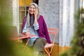 Positive senior lady with glass of water talks on cellphone sitting at table with laptop