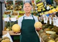 Positive senior male owner of greengrocery shop in apron offering fresh fruits and vegetables Royalty Free Stock Photo