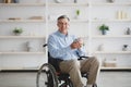 Positive senior man with disability sitting in wheelchair, drinking coffee or tea at home Royalty Free Stock Photo