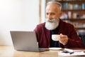 Positive senior man drinking coffee and using laptop Royalty Free Stock Photo