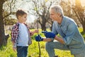 Positive senior man planting tree with his little grandson