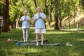 Positive senior man and woman do yoga and meditate on green field