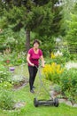 Positive senior woman mowing grass with lawn mower in the garden