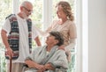 Positive senior woman on wheelchair with caring nurse and elderly friend with walking stick