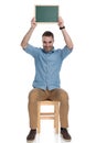 Positive smart casual man holding blackboard above his head, smiling