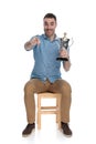 Positive smart casual man holding trophy and pointing forward