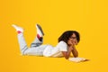 Positive smart teen black curly girl in white t-shirt, glasses reads book, lies on floor