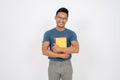 A positive, smiling Asian man is standing on an isolated white background with books in his hand