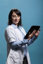 Positive smiling chemistry expert having modern tablet standing on blue background