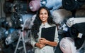 Positive smiling employee with notepad is in the storage full of cloth