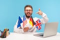 Positive smiling man in eyeglasses holding flags of usa, german, great britain and europe countries, bragging with knowing of many