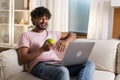 A positive smiling mestizo guy sits in the room on the sofa and enjoys relax after work or study in the cozy home