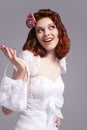 Positive and Smiling Redhaired Caucasian Female Posing in White Wedding Dress and Little Purse Against Gray Background