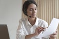 Positive Spanish businesswoman in headset sits at desk having video conference online with partners