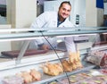 Male shop assistant selling kosher chicken at counter and smiling