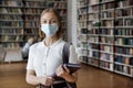 Positive student in face protective mask posing in university library Royalty Free Stock Photo