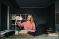 Positive student girl taking selfie while studying at home with a smile on her face, sitting at a table with books and a laptop in Royalty Free Stock Photo