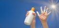 Positive symbol drawing by sunscreen on open hand. Another hand holding a bottle of sun cream. Sky, beams of sun background.