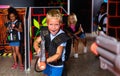 Positive teen boy standing with laser pistol in dark lasertag room during game with friends